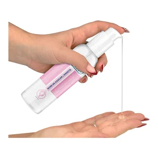 Flacon blanc de lubrifiant avec bande rose et étiquette, versé dans la paume d'une main ouverte sur fond blanc