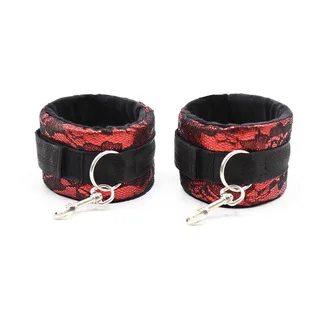 Paire de menottes en velours rouge à motif dentelle noire avec bandes nylon noir et anneaux argentés, sur fond blanc