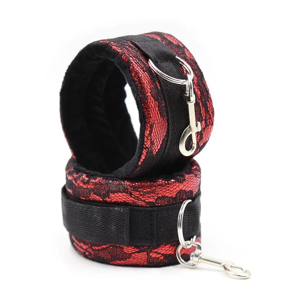 Paire de menottes en velours rouge à motif dentelle noire avec bandes nylon noir et anneaux argentés, sur fond blanc