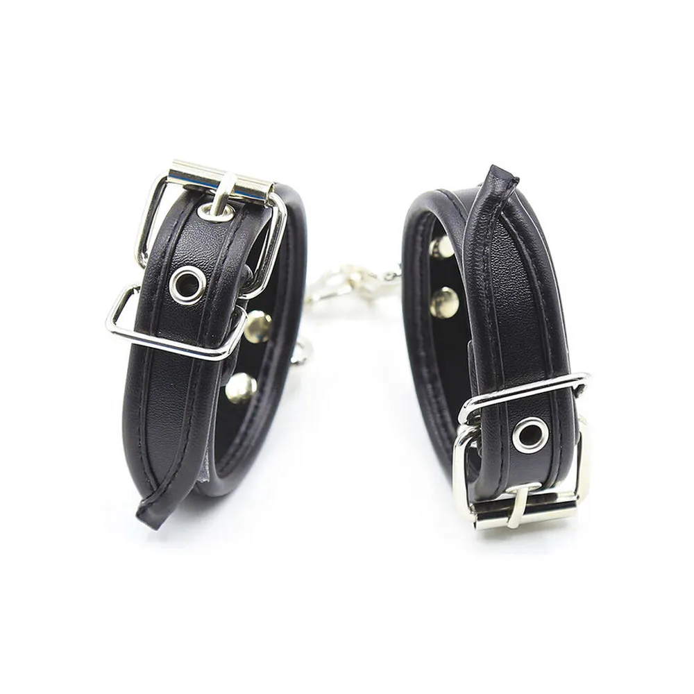 Paire de manchettes de poignets en cuir noir avec boucles métalliques argentées, rivets argentés et mousquetons détachables reliés par une chaîne, sur fond blanc