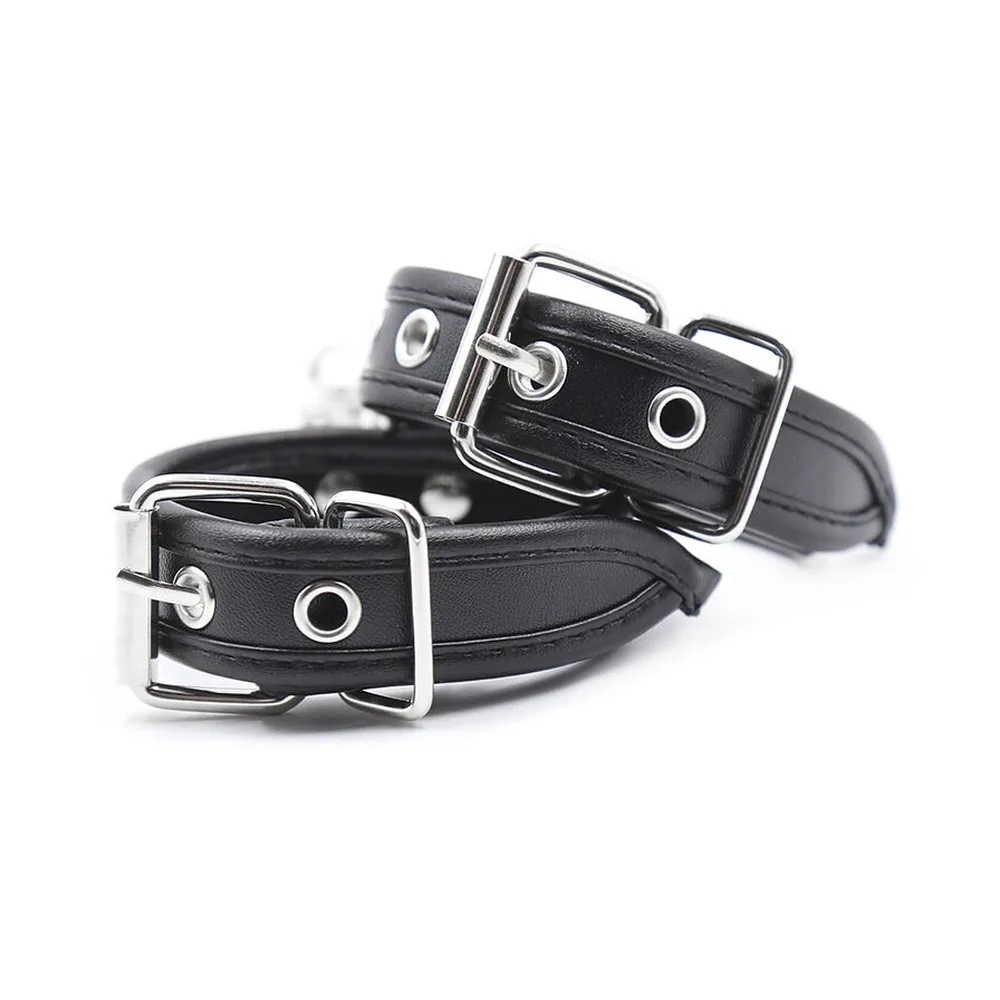 Paire de manchettes de poignets en cuir noir avec boucles métalliques argentées, rivets argentés et mousquetons détachables reliés par une chaîne, sur fond blanc