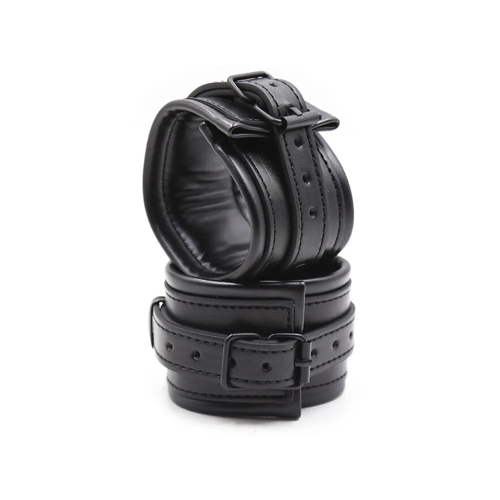 Paire de menottes noires en cuir avec rembourrage, composée d'une bande large à boucle et d'une manchette ajustable reliées par une chaîne, sur fond blanc