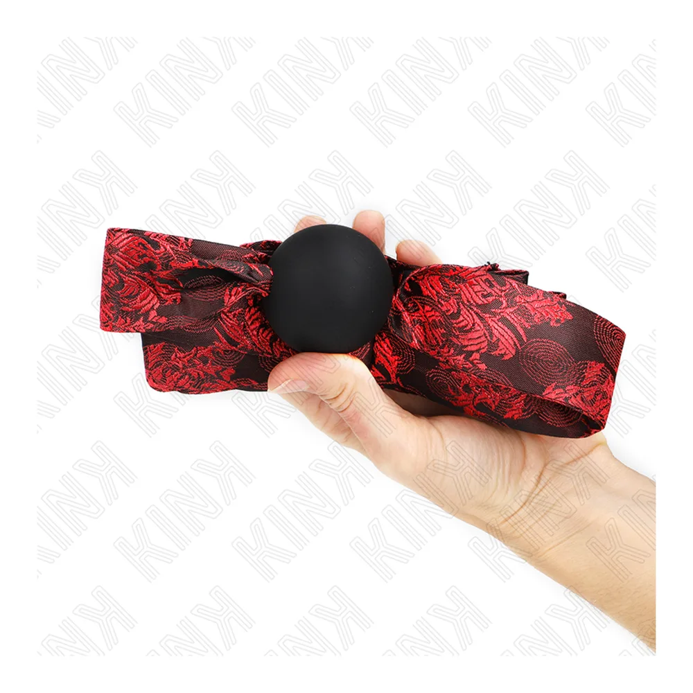 Bâillon boule en silicone noir monté sur un long ruban rouge à motifs floraux noirs, à nouer à l'arrière de la tête