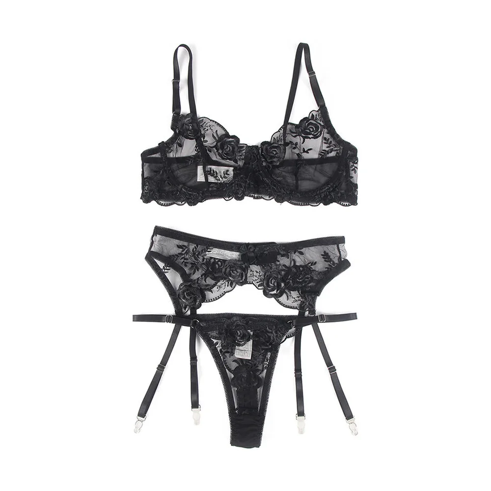 Ensemble trois pièces en dentelle noire florale : soutien-gorge à armatures, string et porte-jarretelles avec détails ajourés, porté sur fond blanc