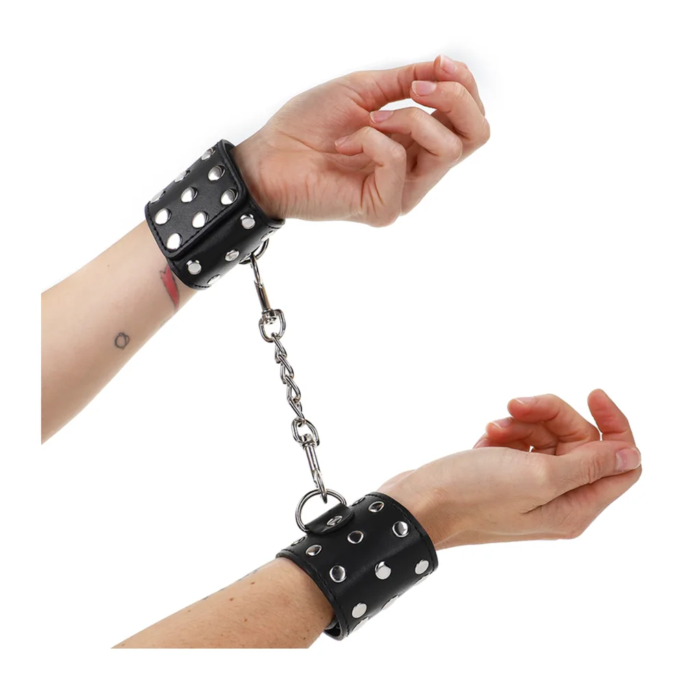 Menottes en cuir noir ornées de rivets argentés, reliées par une chaîne en acier inoxydable avec fermoirs, sur fond blanc
