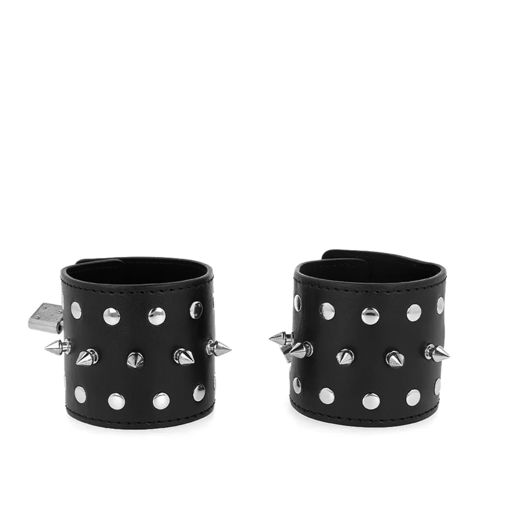 Paire de bracelets noirs en cuir vegan ornés de clous argentés pointus et de rivets ronds, fermés par des cadenas métalliques, vue de face sur fond blanc