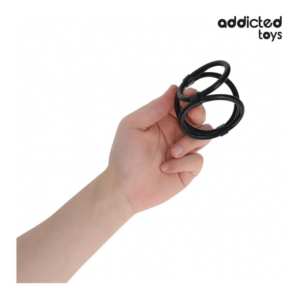 Cockring triple en silicone noir tenu en main, montrant trois anneaux de diamètres différents reliés ensemble sur fond blanc