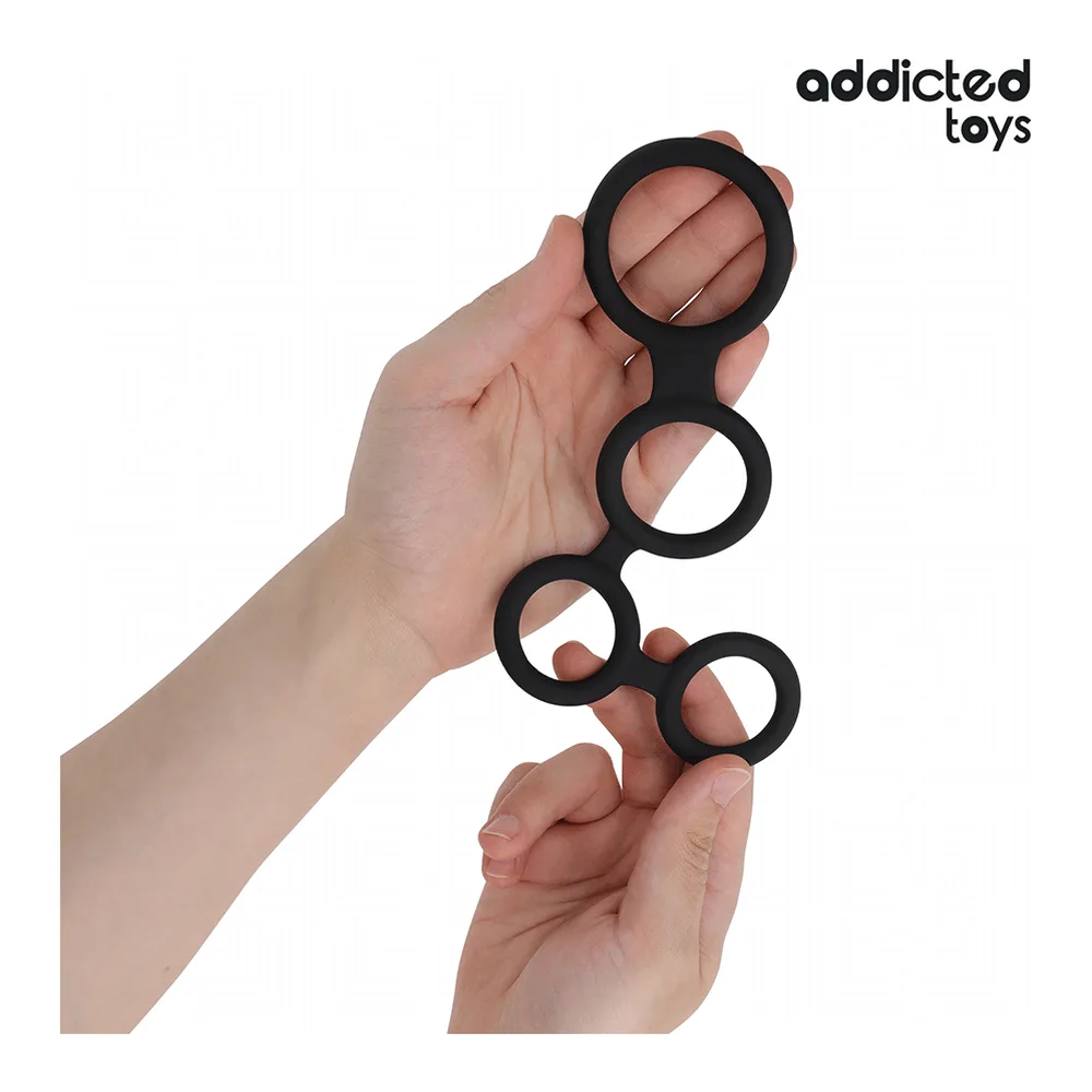 Cockring composé de quatre anneaux noirs en silicone reliés en colonne, tenu en main sur fond blanc