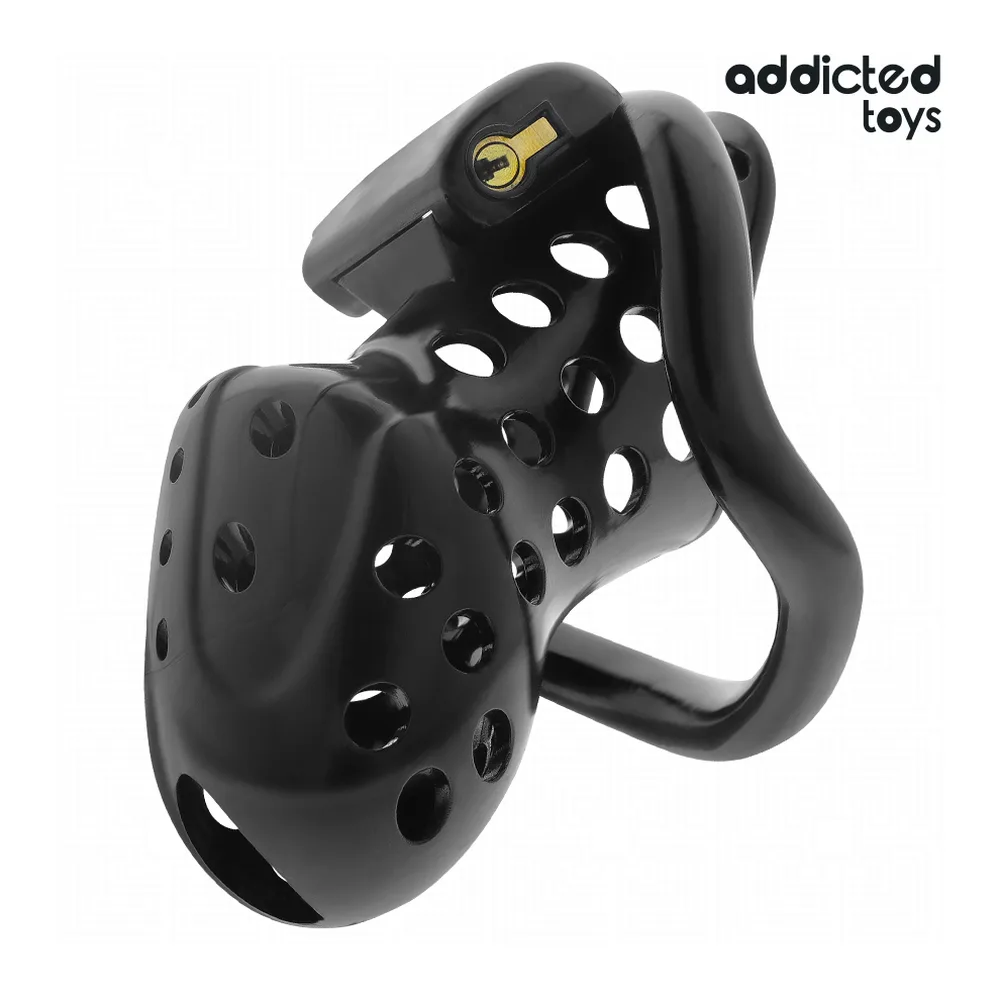 Cage de chasteté noire avec perforations ajourées et anneau d'attache doré, présentée hors de son emballage blanc et noir Addicted Toys aux côtés de sa boîte