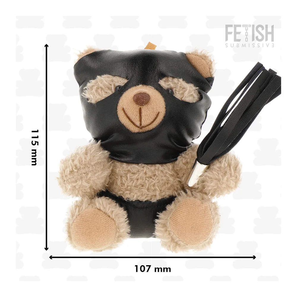 Peluche ours beige et noir avec masque en cuir noir sur le museau, oreilles en dentelle beige, tenant un fouet à lanières noires, sur fond blanc