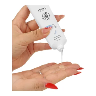 Tube blanc de lubrifiant Bruma à l'aloe vera versant son gel transparent dans une main, ongles rouges, sur fond blanc