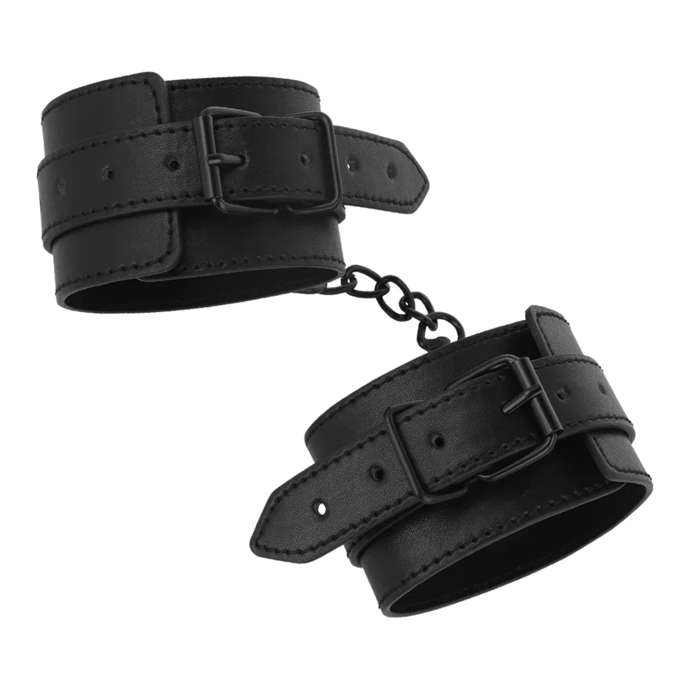 Paire de manchettes de chevilles en cuir végétalien noir avec rivets, fermées par boucles et reliées par une chaîne métallique, sur fond blanc
