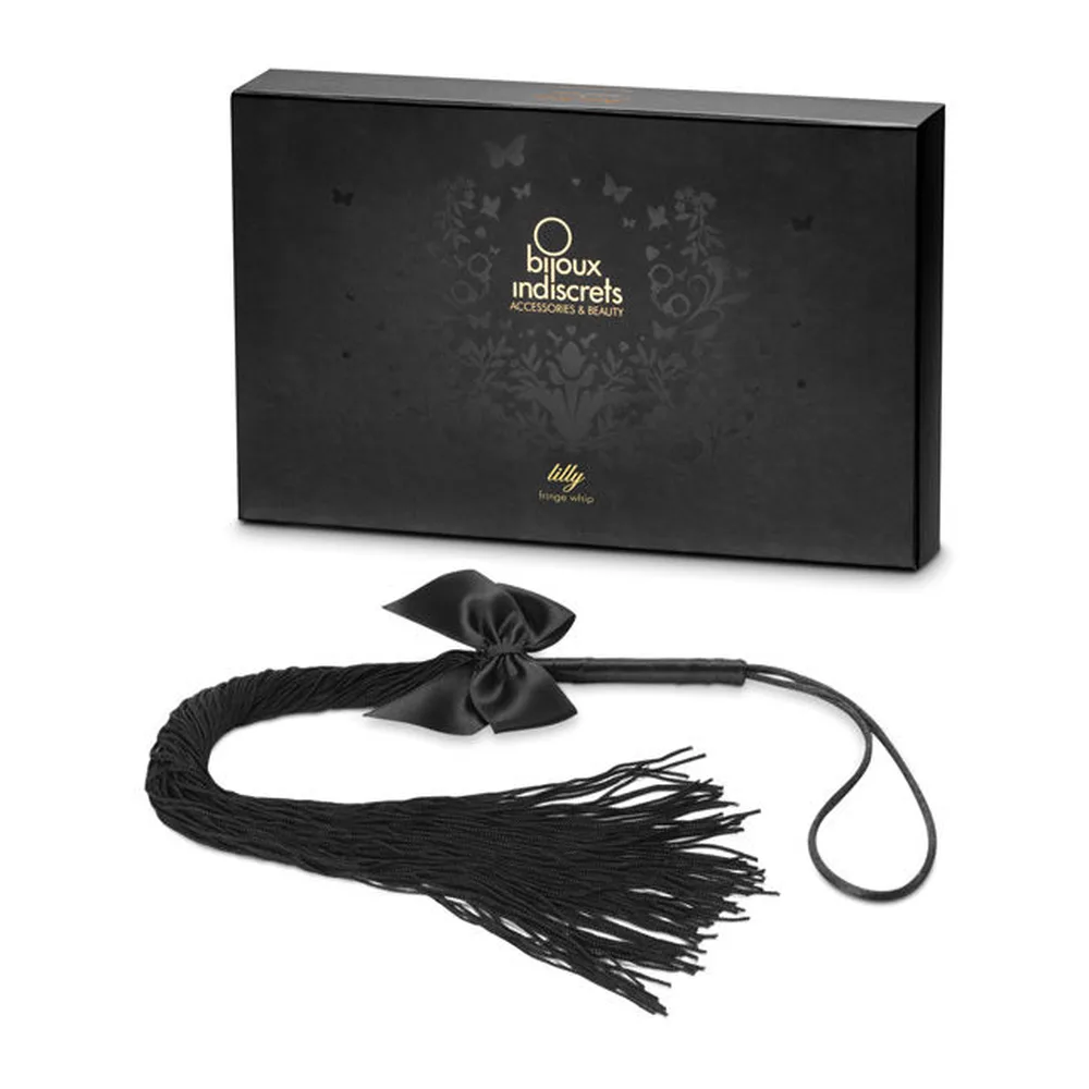 Fouet à franges noires textiles avec nœud de soie, livré dans son coffret noir Bijoux Indiscrets de la gamme Lilly, présenté ouvert avec le produit en avant