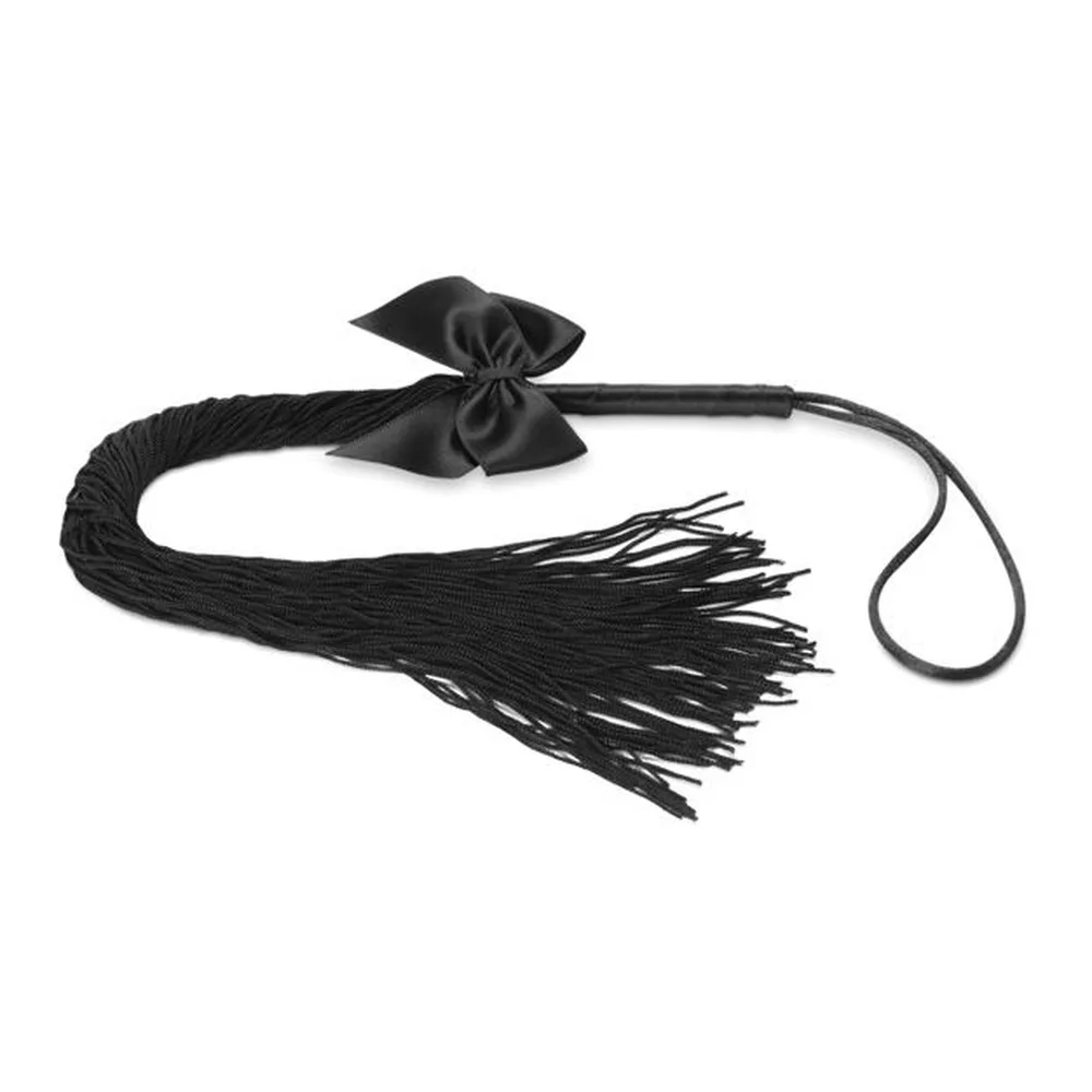 Fouet à franges noires textiles avec nœud de soie, livré dans son coffret noir Bijoux Indiscrets de la gamme Lilly, présenté ouvert avec le produit en avant