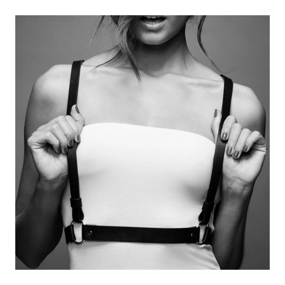 Harnais noir en cuir synthétique avec deux bandes croisées et une ceinture inférieure ornée de rivets dorés et d'anneaux métalliques, sur fond blanc