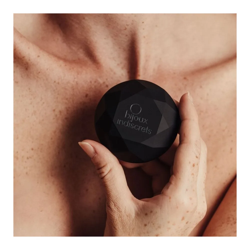 Vibrateur noir mat aux facettes géométriques en forme de diamant, posé sur une surface blanche avec reflet