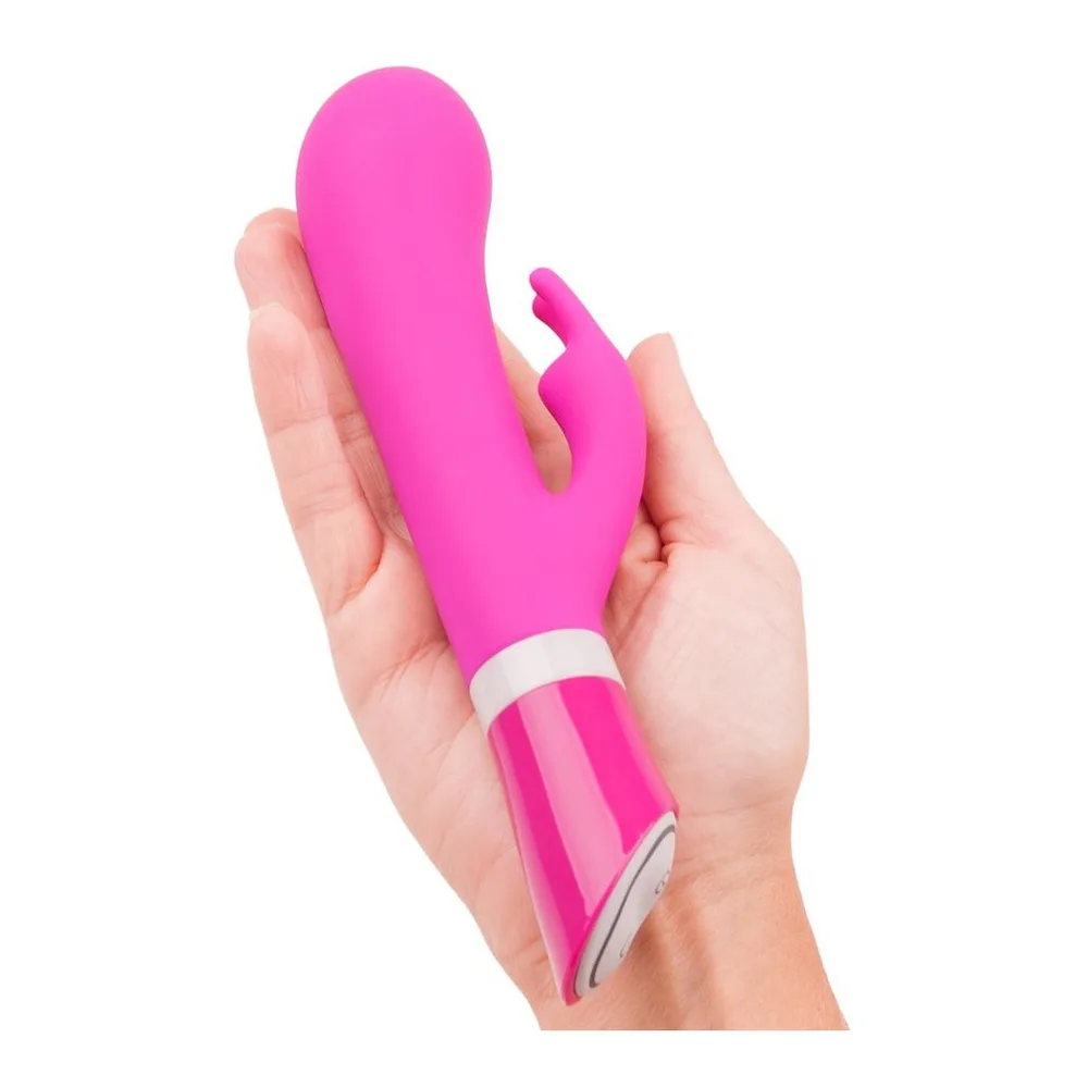 Vibromasseur rabbit rose fuchsia en silicone, tenu en main, avec bras clitoridien articulé et bande blanche au niveau de la base