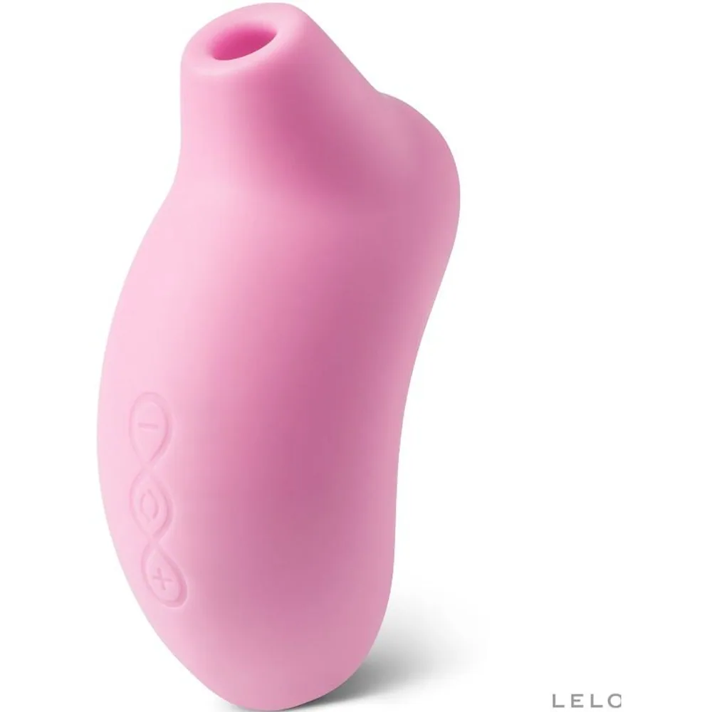 Stimulateur clitoridien rose pâle au design ergonomique bombé, présenté dans son emballage noir avec accessoires : câble USB blanc, pochette de rangement noire et carte de garantie