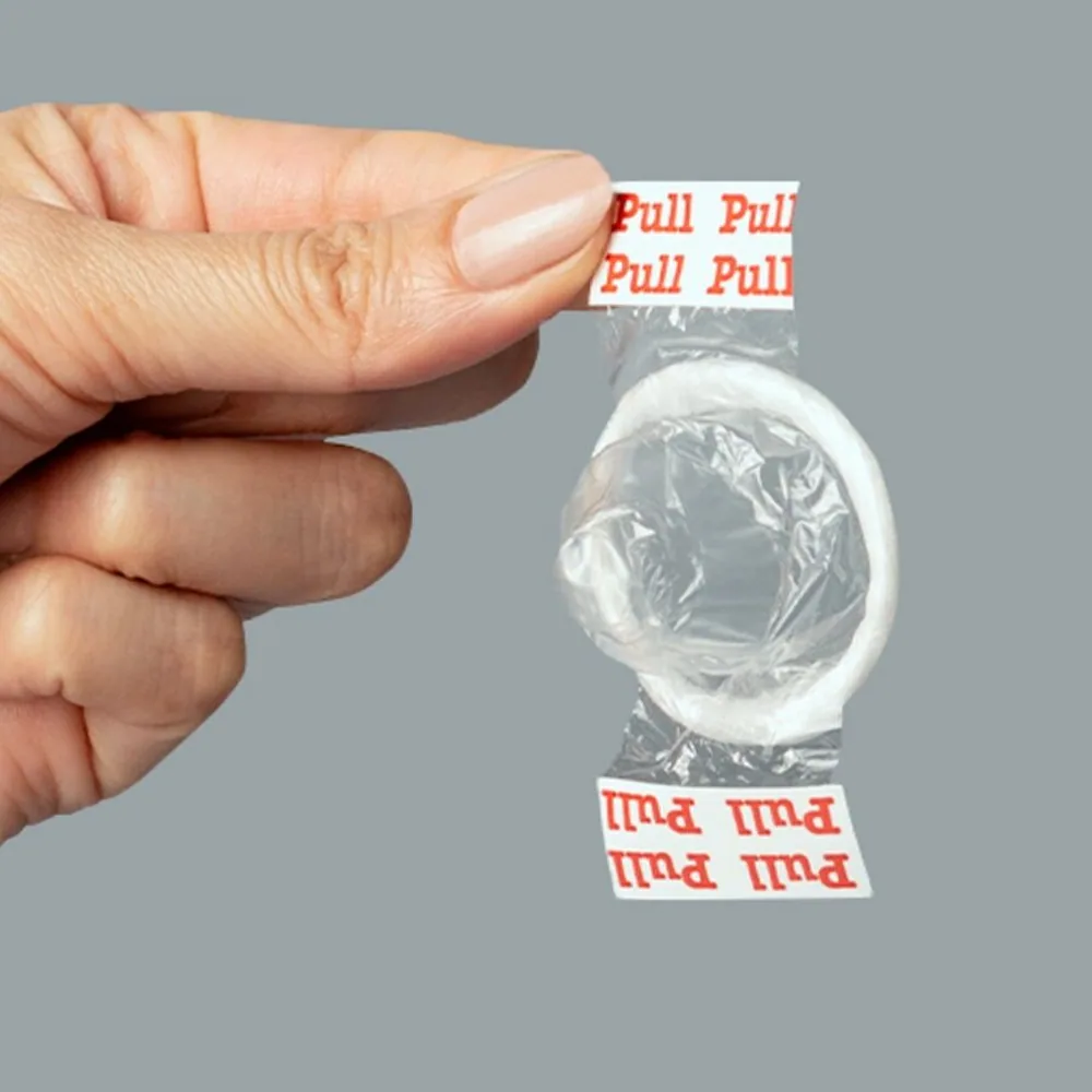 Emballage noir et doré de préservatifs Uniq Pull avec un sachet transparent montrant un préservatif transparent, et une main démontrant le système de bandes à tirer pour le déploiement