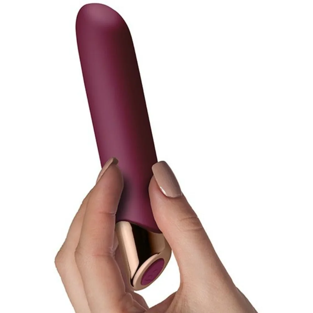 Vibromasseur cylindrique bordeaux à pointe effilée et base dorée, posé sur fond blanc avec reflet miroir