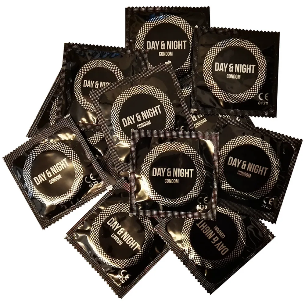 Plusieurs sachets individuels de préservatifs Day & Night à motif damier noir et blanc, empilés en vrac sur fond blanc