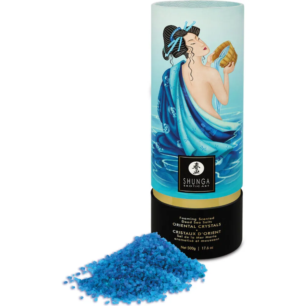 Cristaux de sel de bain bleu vif étalés au premier plan, avec derrière le tube cylindrique de présentation bleu pâle orné d'une illustration de femme aux cheveux noirs et drapé bleu turquoise, logo Shunga et bandeau doré à la base