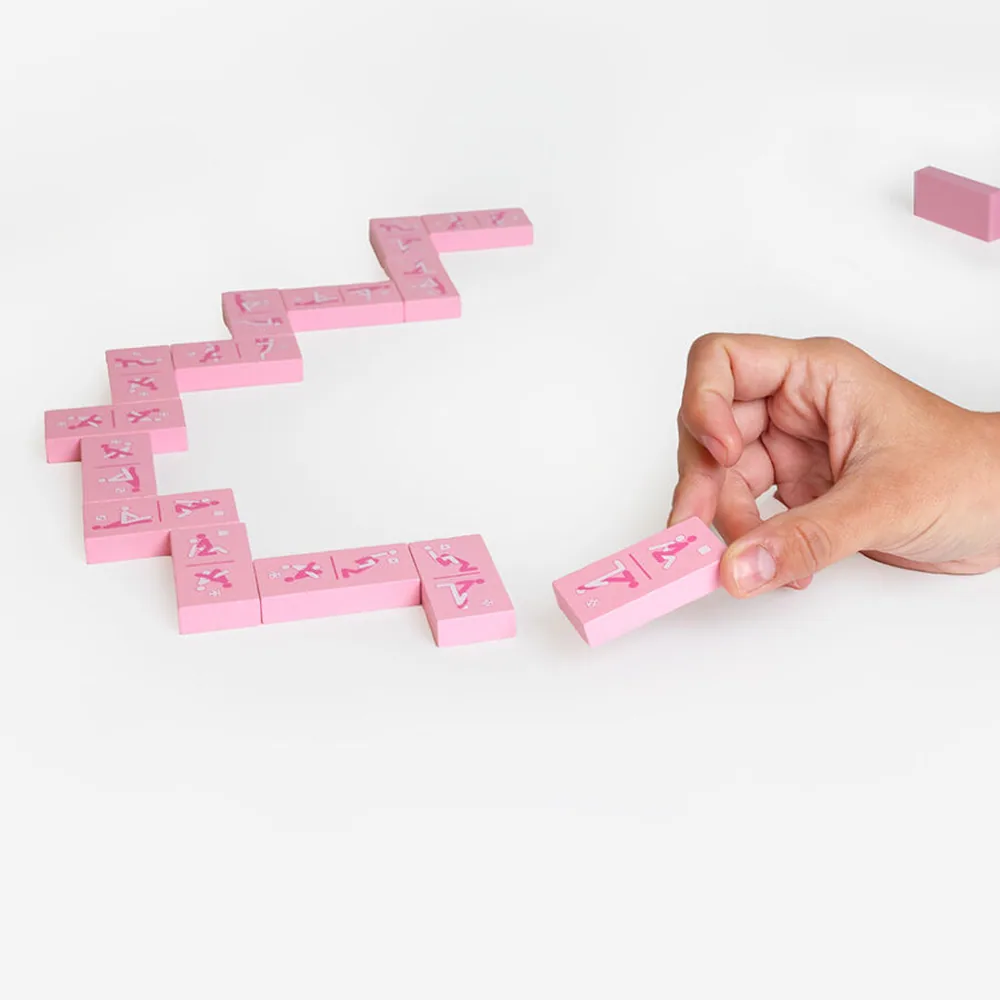 Boîte de jeu Kinky Domino rose avec logo, accompagnée de dominos rose pâle gravés de symboles, vue de l'ensemble du produit et de son emballage